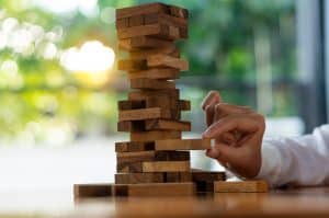 hand tried to pull out the wooden block from a tall tower of blocks